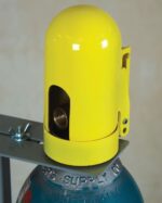 A close-up of a yellow Snapcap, partially revealing a coiled connection inside, secured to a metal bracket atop a gray gas cylinder. The focus is on the protective Justrite Gcyl Acc, Snapcap, Hpft and its attachment.
