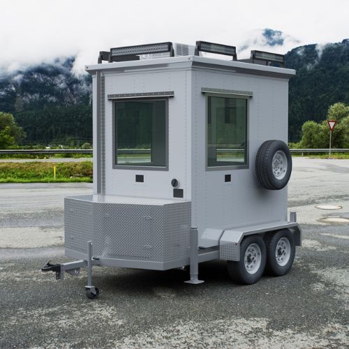 A small, mobile guard booth on a dual-axle trailer offers flexible security structures. It features large windows, a spare tire on the side, and a storage compartment at the front. Clouds partially cover the mountains in the background.