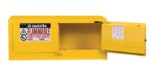 The yellow Justrite Flam Pigy 12G cabinet stands open, showcasing a FLAMMABLE KEEP FIRE AWAY warning label. The interior is empty with additional safety labels visible on the door.