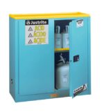 A blue Justrite Cabinet, model Acid Sfty 30G Man Blu, with a yellow top is partially open, revealing plastic containers inside. The door is labeled with caution signs and ACID in various languages for universal safety and clarity.