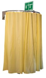 A yellow emergency shower with a partially open circular Modcurtain, wall-mounted and embodying Justrite Ssaccys commitment to safety and innovation, is complemented by a ceiling-suspended rail. Above it, a green safety sign displays symbols for eyewash and shower stations.