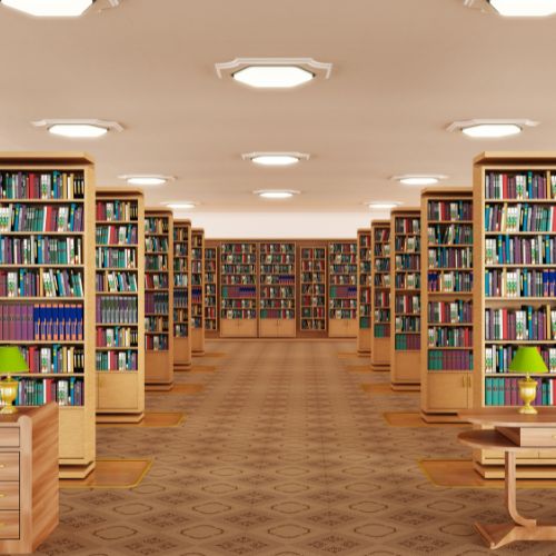 A spacious library interior features electric mobile shelving filled with colorful books. The shelves are symmetrically arranged, and warm overhead lighting illuminates the room. Tables with green lamps are placed along the aisle, enhancing a perfect reading ambiance.
