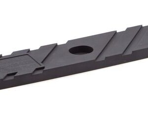 The Justrite Chock, model Acc 3010, is a black rectangular plastic strip featuring two large circular holes at each end and a smaller central pattern with diagonal lines and a hexagonal shape.