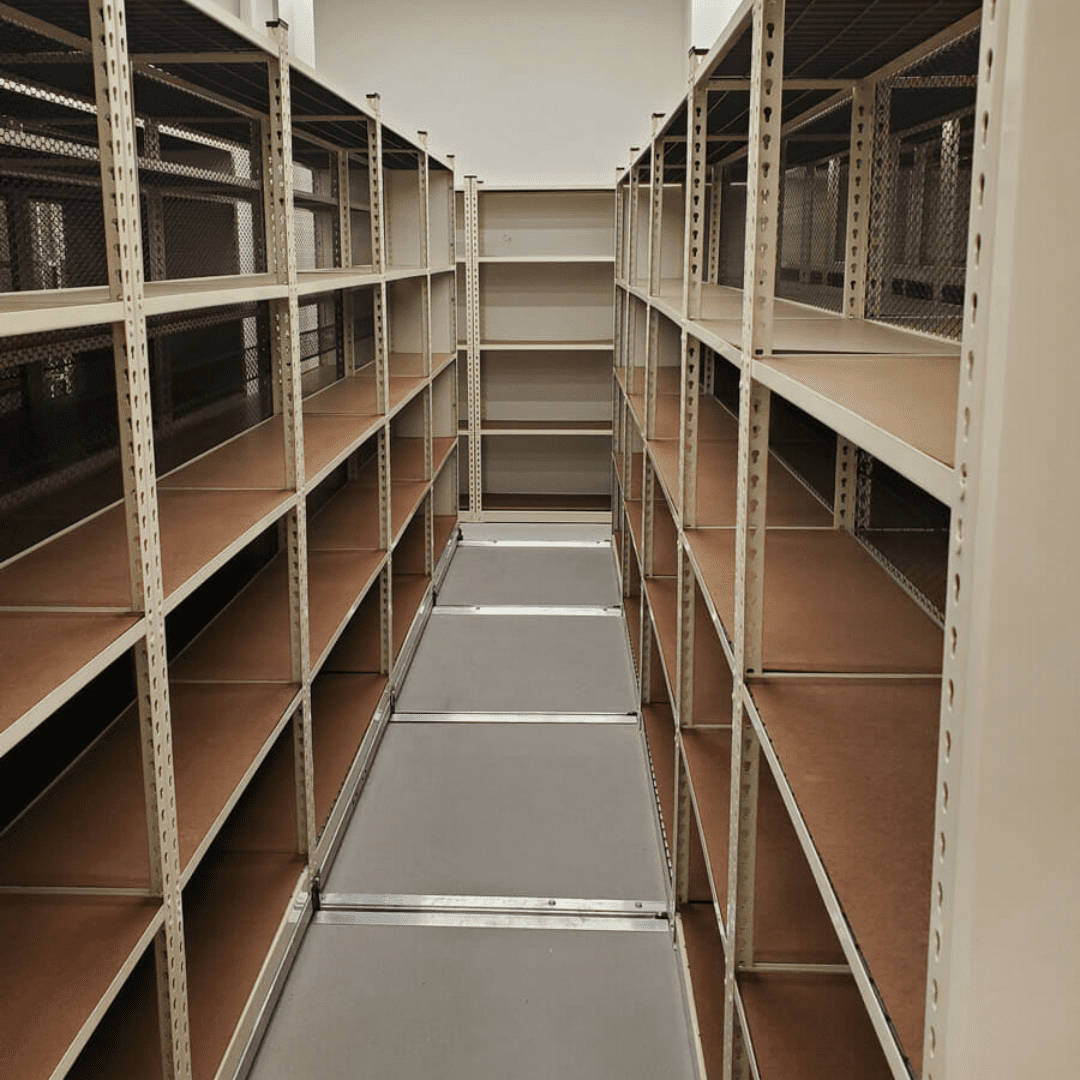 Empty metal shelving units in a narrow aisle, with brown shelves and a smooth gray floor, offer efficient pallet racking for moving companies. The shelves stretch toward the back wall, maximizing storage potential and depth in the space.