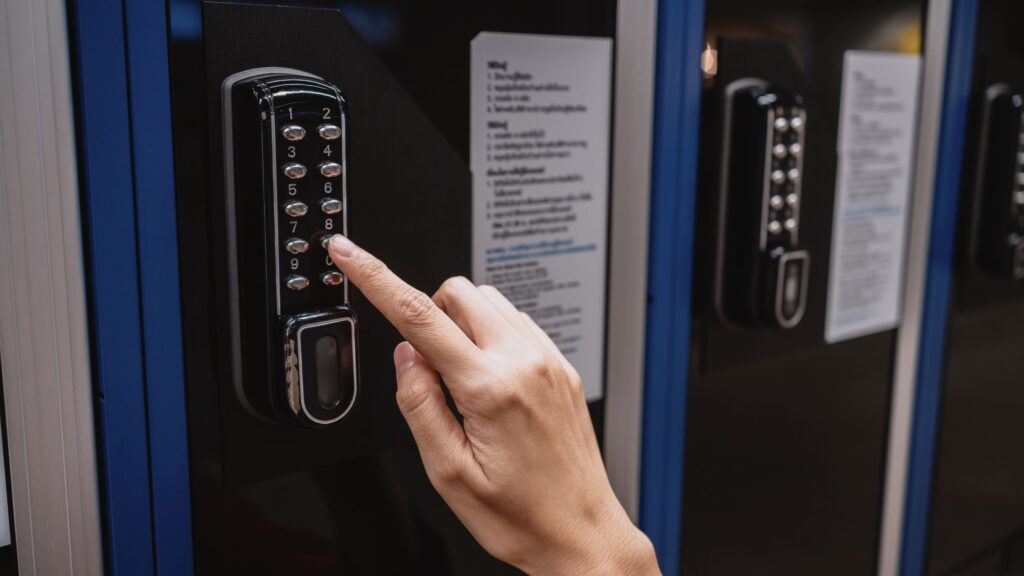 A hand is pressing buttons on a digital combination lock attached to a dark-colored locker, showcasing the convenience of Pin Code Access Lockers. The lock features a numeric keypad and a curved handle at the bottom, with other similar keyless locker systems visible in the background.