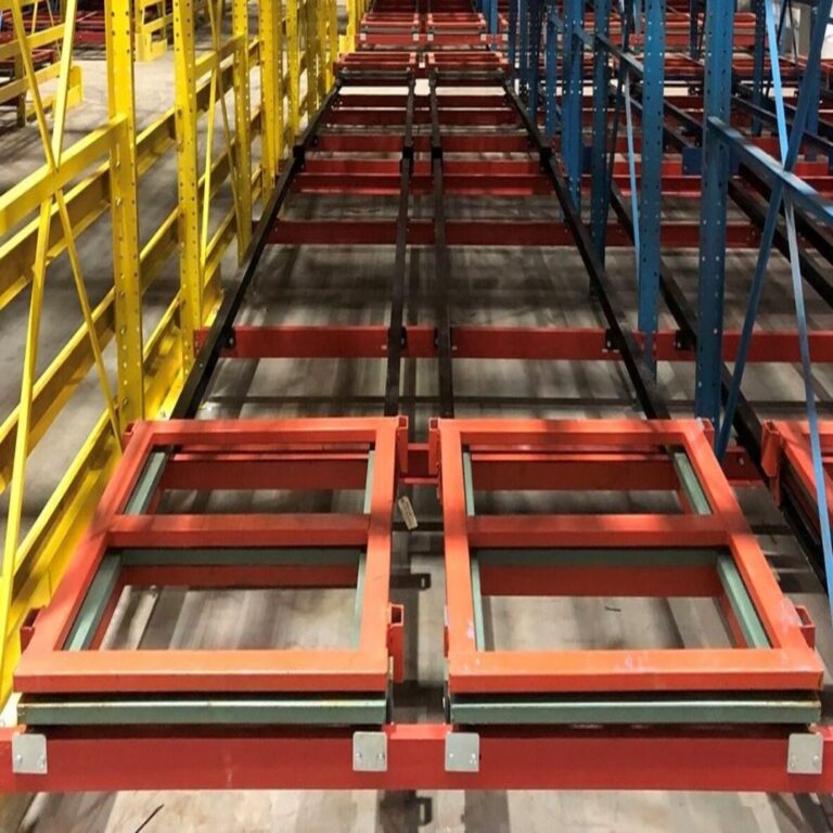 Warehouse storage racks feature two red, square metal frames on tracks. The yellow and blue racks create aisles with no items stored on them, illustrating a comprehensive guide to selecting pallet racks. The concrete floor adds to the industrial feel.