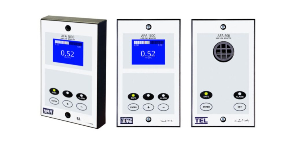 Three digital airflow monitors, essential for Fume Hood Technology, feature blue displays showing 0.52. Each monitor has black buttons labeled Enter, Mute, and Alarm. The middle and left monitors display AFA 1000, while the right one reads AFA 500, enhancing Laboratory Safety Equipment.