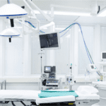 A modern, sterile operating room embodies the pinnacle of healthcare, featuring an empty surgical table, overhead lights, and cutting-edge medical equipment. A monitor displays vital information while various devices are connected, with tubes and machines poised for action.