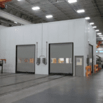 The interior of a large industrial facility resembles a modern healthcare environment, featuring a white, windowless structure with two large closed roller doors and a small entry door. The high ceiling boasts visible metal beams and lighting, while the smooth floor is designed for efficiency and cleanliness.