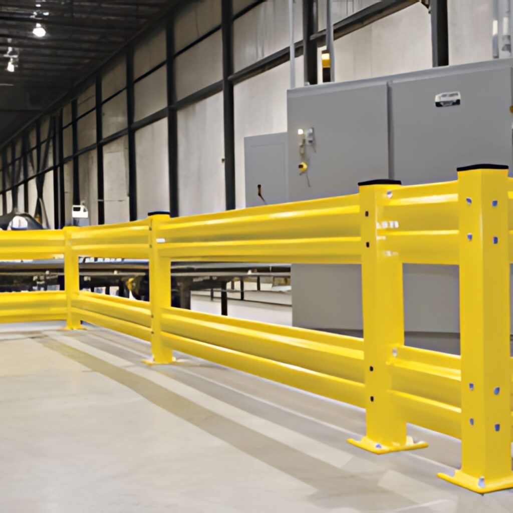 A brightly lit industrial Cogan warehouse interior features sturdy yellow safety barriers. Positioned in front of large gray machinery, these barriers complement the high ceilings and concrete floor visible in the background.