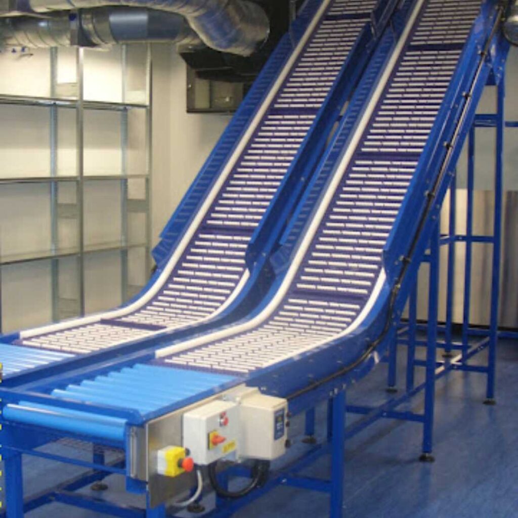 Two blue AmbaFlex Conveyors with a series of steps or ridges are positioned side by side, sloping upwards within an industrial setting. The room features blue flooring and visible metal shelves in the background.