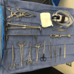A set of surgical instruments lays out on a blue cloth, embodying the precision of healthcare. The tools—scissors, forceps, clamps, and retractors—along with a rolled gauze pad and tubing, are neatly organized for a medical procedure.