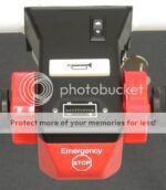 The emergency STOP button panel on the Electro Kinetic Technologies Pony Express Motorized Platform Truck, with a 1500 lb. capacity and a deck size of 49 L x 25.5 W, has Emergency inscribed above STOP on its red surface and includes a keyhole, switch, and USB-like port.