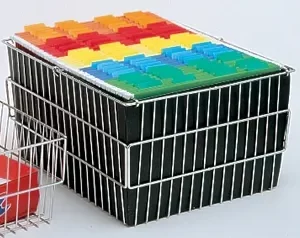 A metal filing basket, similar to those used in the Electro Kinetic Techs. Pony Express Cart (Part MMC-SM01), holds several black folders with orange, yellow, blue, and green tabs. It sits against a neutral backdrop with another basket partially visible on the left.