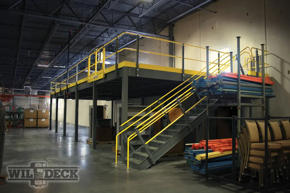 A warehouse interior featuring a raised mezzanine platform with yellow railings and a staircase. Beneath, Utah lockers offer storage solutions, while to the right, colorful metal beams and panels are stacked. A logo is visible on the bottom left.