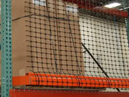 In a warehouse setting, stacks of large cardboard boxes are carefully secured on an orange pallet rack, enhanced by the protective grid of pallet rack safety netting.