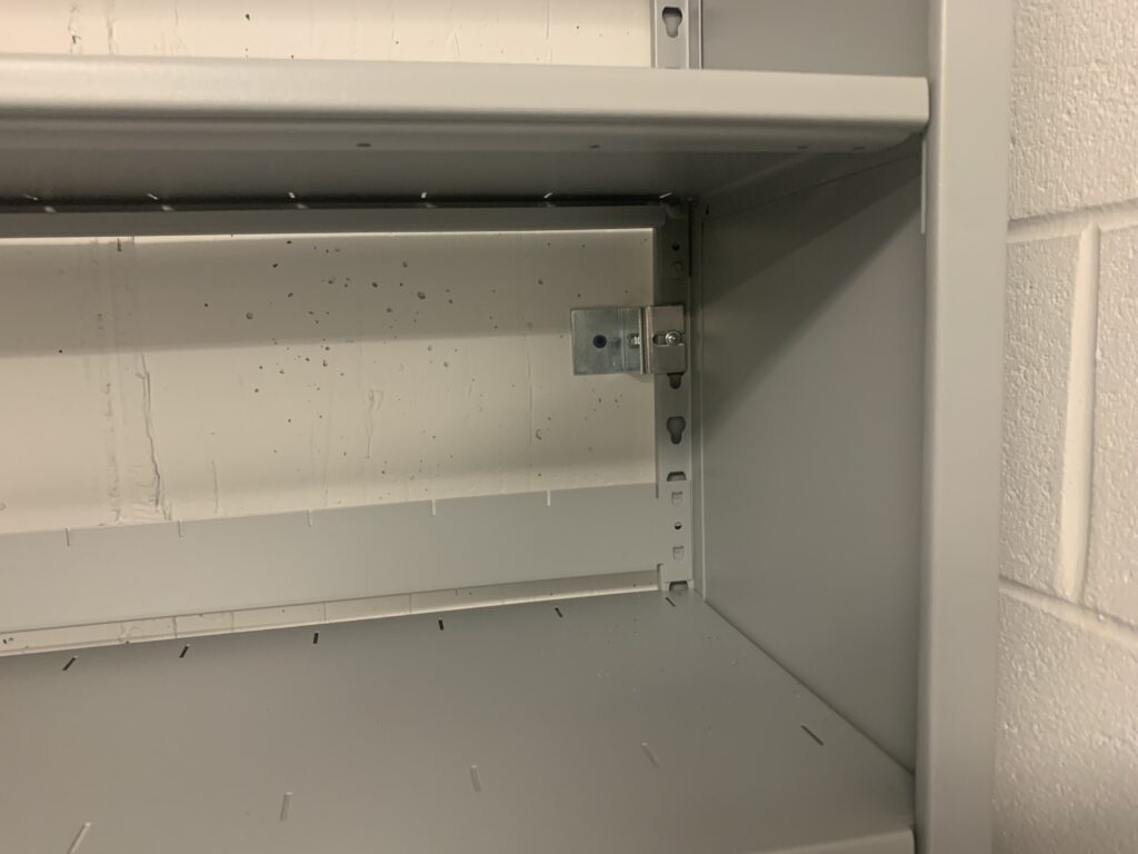 Empty metal shelves inside a storage unit demonstrate efficient storage with sturdy mounting brackets. A plain white brick wall on the right completes this simple yet practical space, ideal for those considering Utah mobile shelving solutions.