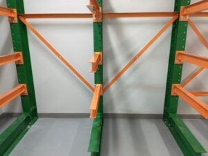 Empty green and orange metal shelving units stand in a storage room with a gray floor and white walls—an ideal canvas for implementing lumber storage solutions fit for a junior high school.