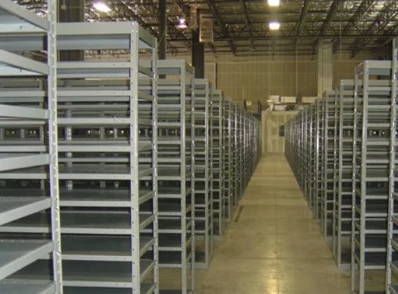 The wide, empty warehouse boasts rows of metal shelving units lining both sides of a central aisle. This industrial setting, with its high ceilings and fluorescent lighting, creates an expansive and orderly appearance.
