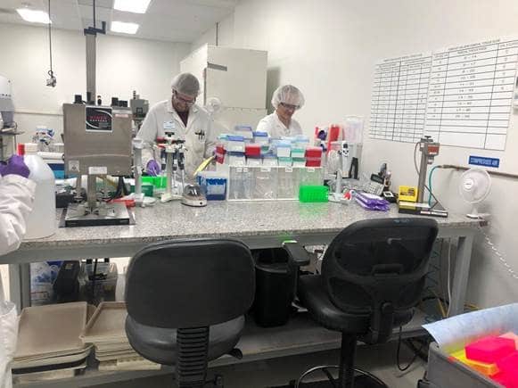In dynamic lab environments, scientists in lab coats and hairnets focus at a laboratory bench adorned with Premium Laboratory Casework and Custom Tables. Equipment, containers, and colorful trays surround them as charts cover the whiteboard behind their technical workstations built for precision.