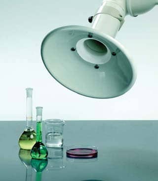 A laboratory setup showcases a fume hood paired with advanced fume extraction systems. Two conical flasks filled with green and yellow liquids, a glass beaker, and a petri dish rest elegantly on a reflective surface.