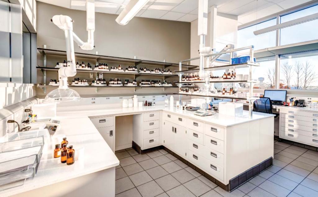 A brightly lit process research lab with white countertops and cabinets. Shelves hold small bottles, and various lab equipment is scattered around. Large windows allow natural light to illuminate the space, supporting quality control in distilleries like Brown-Formans comprehensive setups.