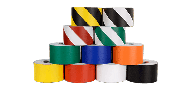A pyramid stack of color-coded tape rolls serves as a vital tool for warehouse organization and safety. The top row features yellow and black, black and white tapes, with a middle row of red, green striped in white. The bottom displays green, blue, orange, yellow, white, and black rolls with wide stripe patterns.