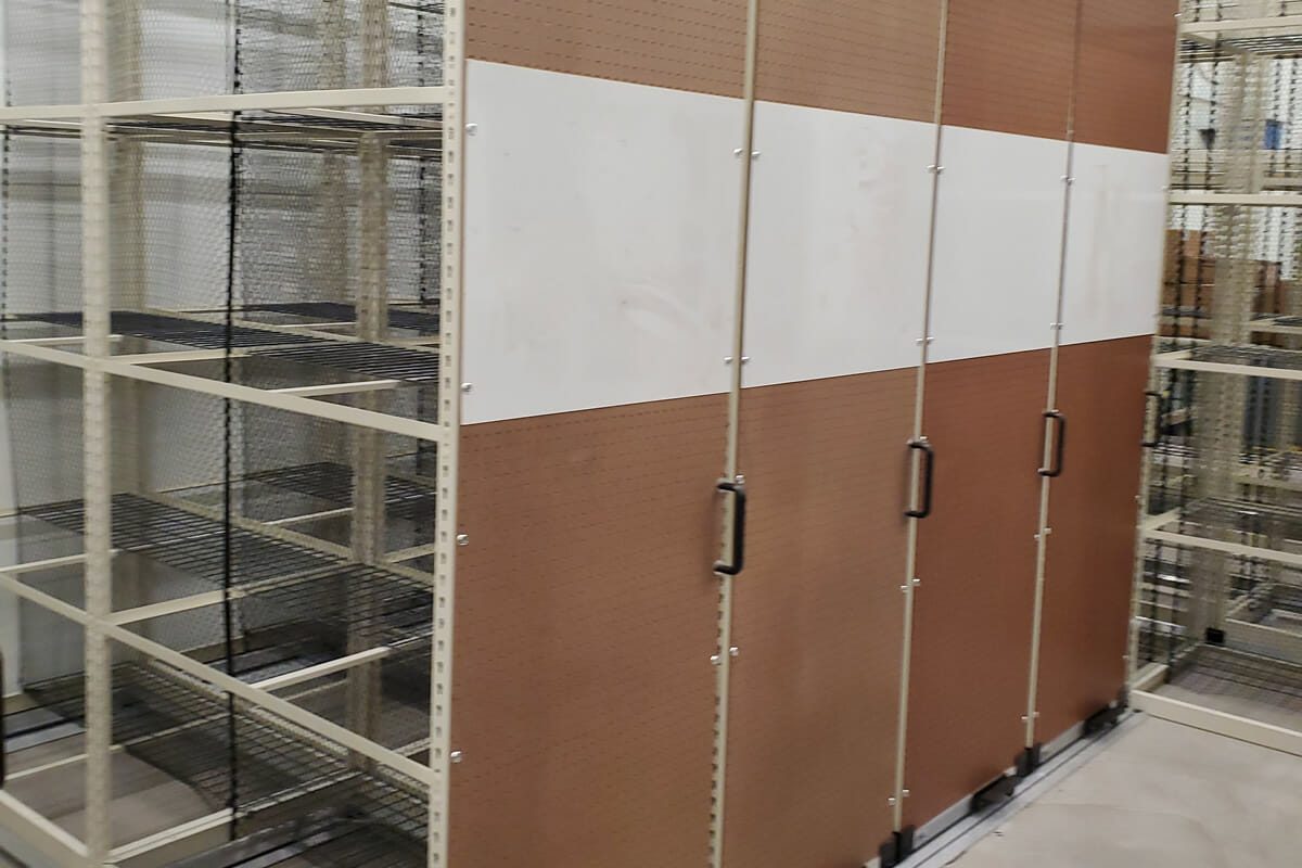 Empty metal shelves with brown sliding doors in a storage or industrial space offer Food Service Shelving Solutions. Featuring handles for easy access, the concrete-floored area appears well-organized and spacious.