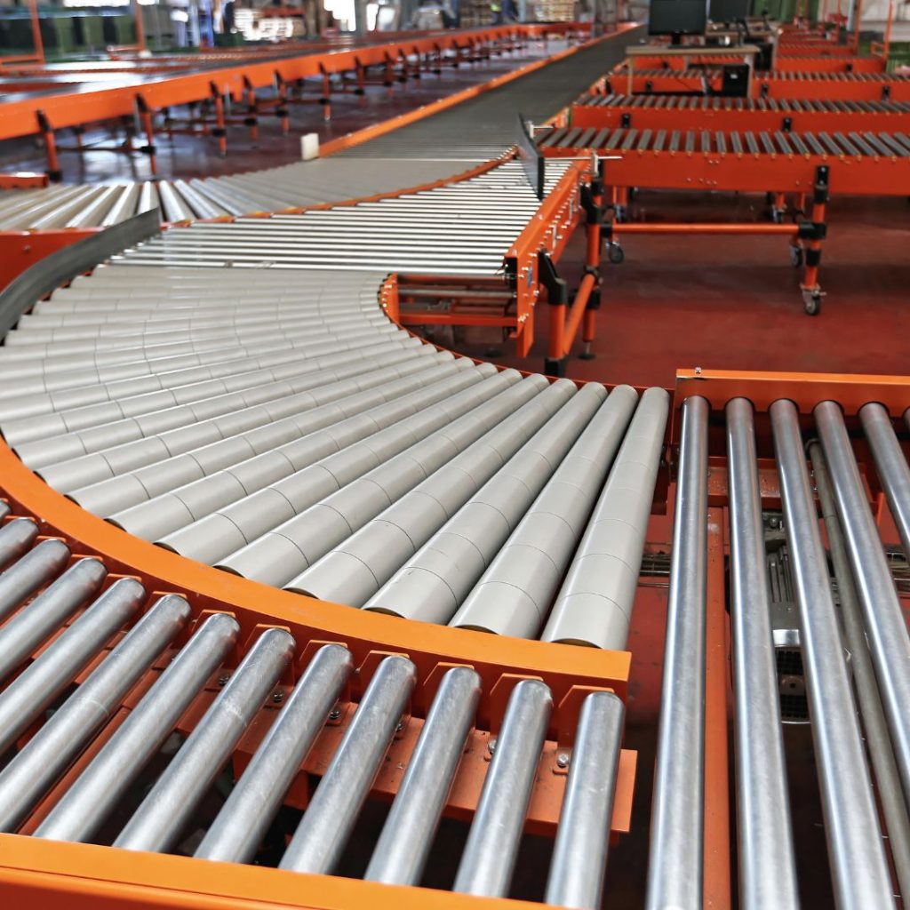 In the mining and gas department, a conveyor system with silver rollers and orange frames elegantly curves through an industrial setting. The semi-circular roller arrangement on the polished reddish floor highlights a clean and organized environment.