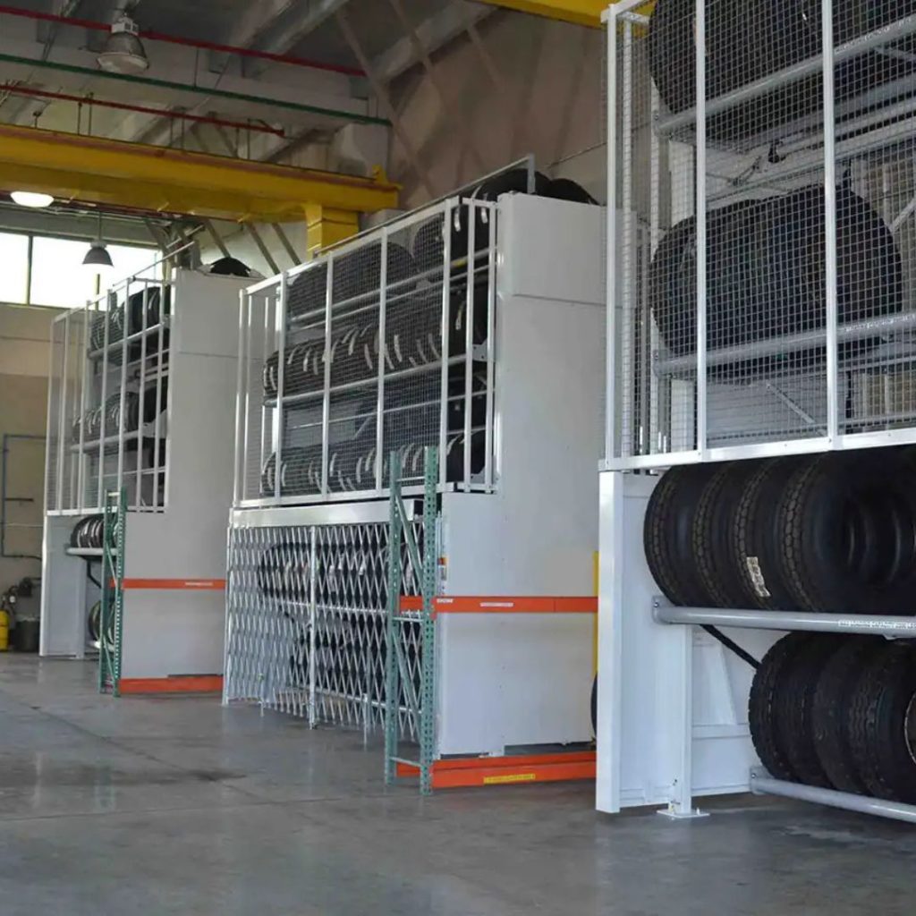 Tire storage in a warehouse features large, vertical racks filled with various types of tires. The department: mining and gas ensures the racks with mesh doors are securely organized. Ladders allow access, while overhead yellow cranes stand ready. The floor remains clear and spacious.