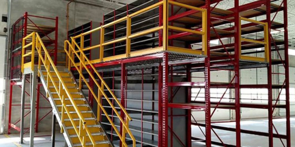 A warehouse mezzanine with yellow stairs and platforms is shown, featuring Equipto Brochures on the red and yellow railings. The metal structure includes industrial shelving units, and the setting is well-lit with concrete walls in the background.