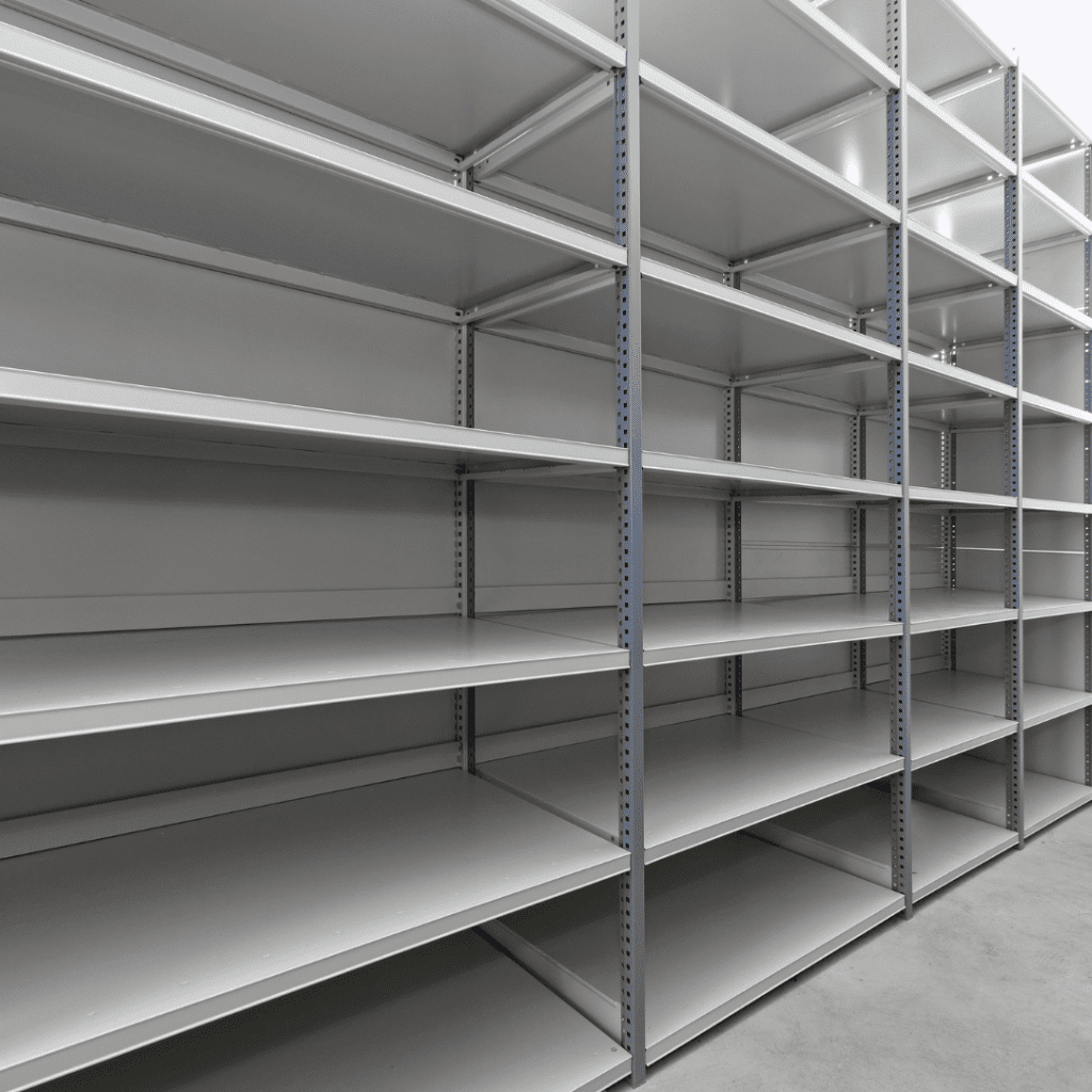 Empty industrial metal shelving units, perfect for material handling, are arranged in a warehouse setting and extend into the distance. The uniformly gray shelves feature several levels, creating a repetitive pattern against the concrete floor, reminiscent of a gallerys organized layout.