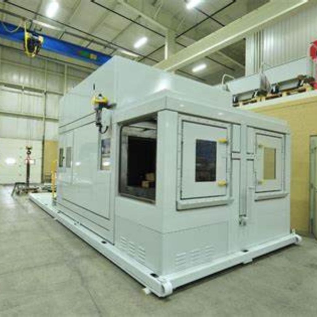 A large white industrial machine stands inside a spacious factory with high ceilings, likely belonging to the Mining and Gas department. With multiple doors and windows, it seems designed for manufacturing or testing purposes.