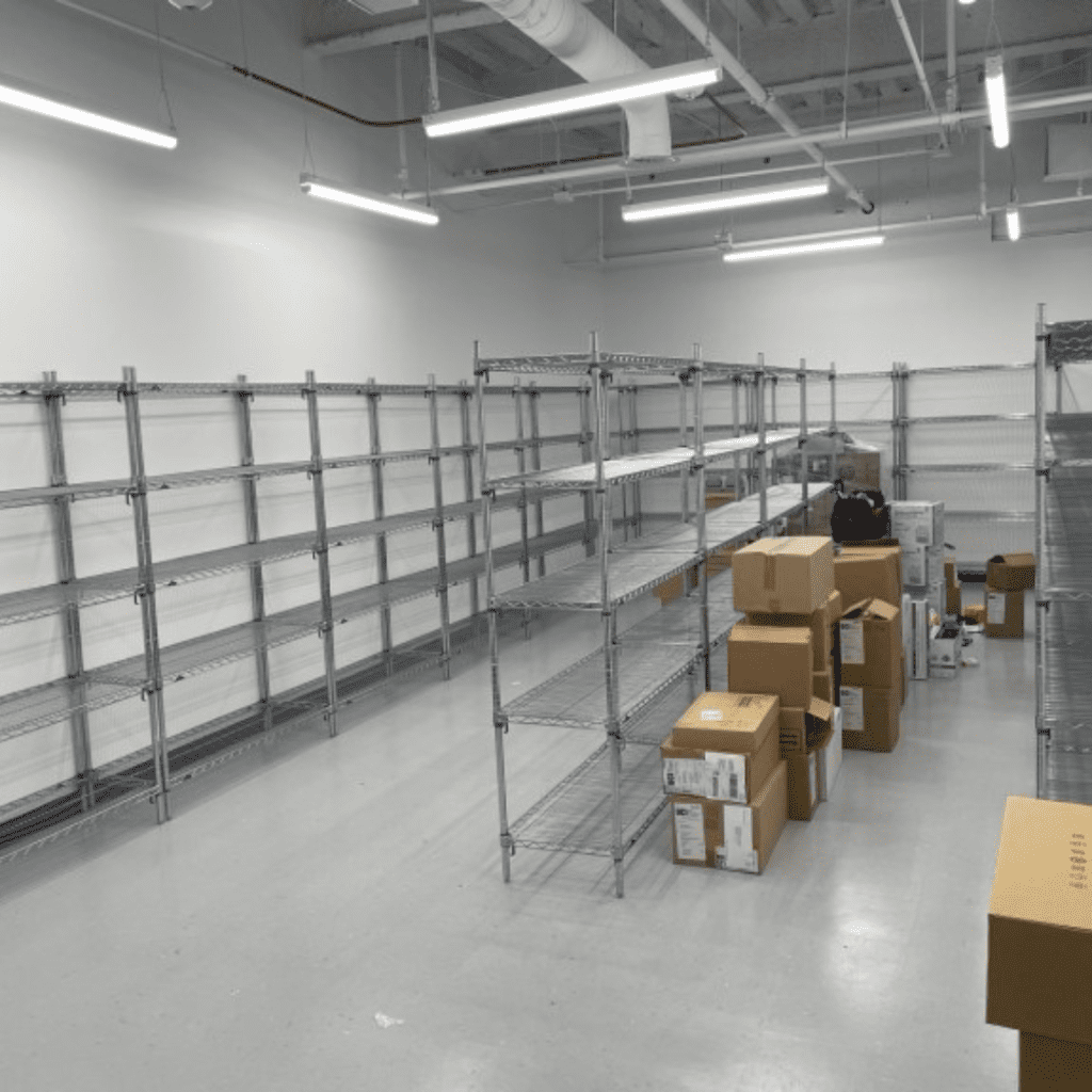 A room with metal shelving units lines the white walls, mostly empty like a material handling space. Cardboard boxes of various sizes=