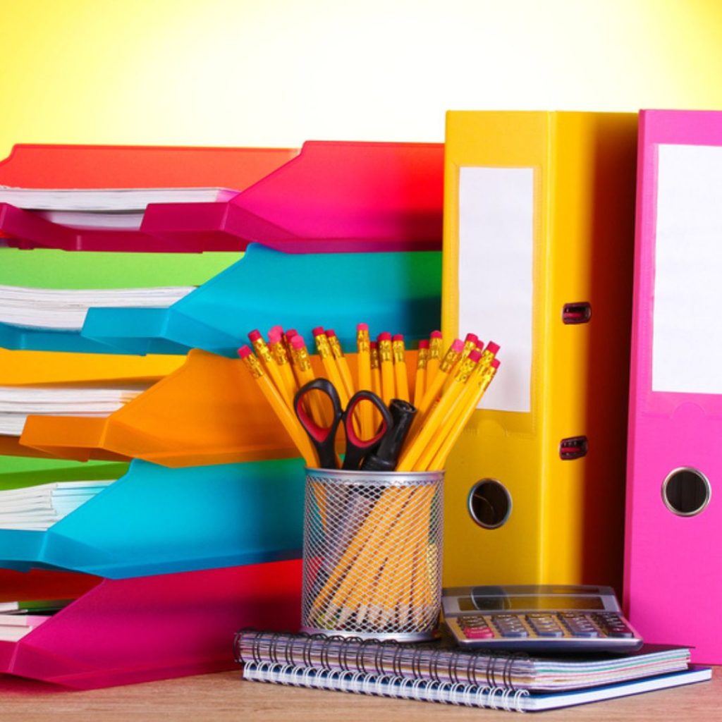 A colorful arrangement of office supplies creates an inspiring Department of Education workspace. Vibrant folders, binders, and notebooks are stacked on a desk. A metal cup holds pencils and scissors, while a calculator adds practicality against a bright background.