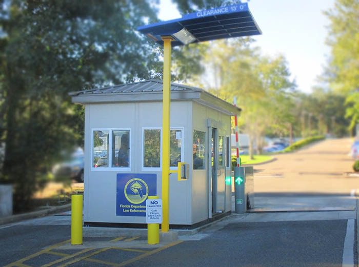A small security booth at the entrance of a parking area, with a sign reading Florida Department of Law Enforcement, doubles as an industrial equipment enclosure. Its surrounded by trees, featuring a height clearance sign and various secure equipment visibly protected within.