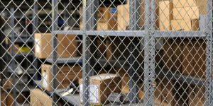 A storage room at Hill Air Force Base features metal shelving units filled with cardboard boxes and items. In the foreground, security cages made of a chain-link fence partially obscure the view, ensuring an extra layer of protection for the stored contents.