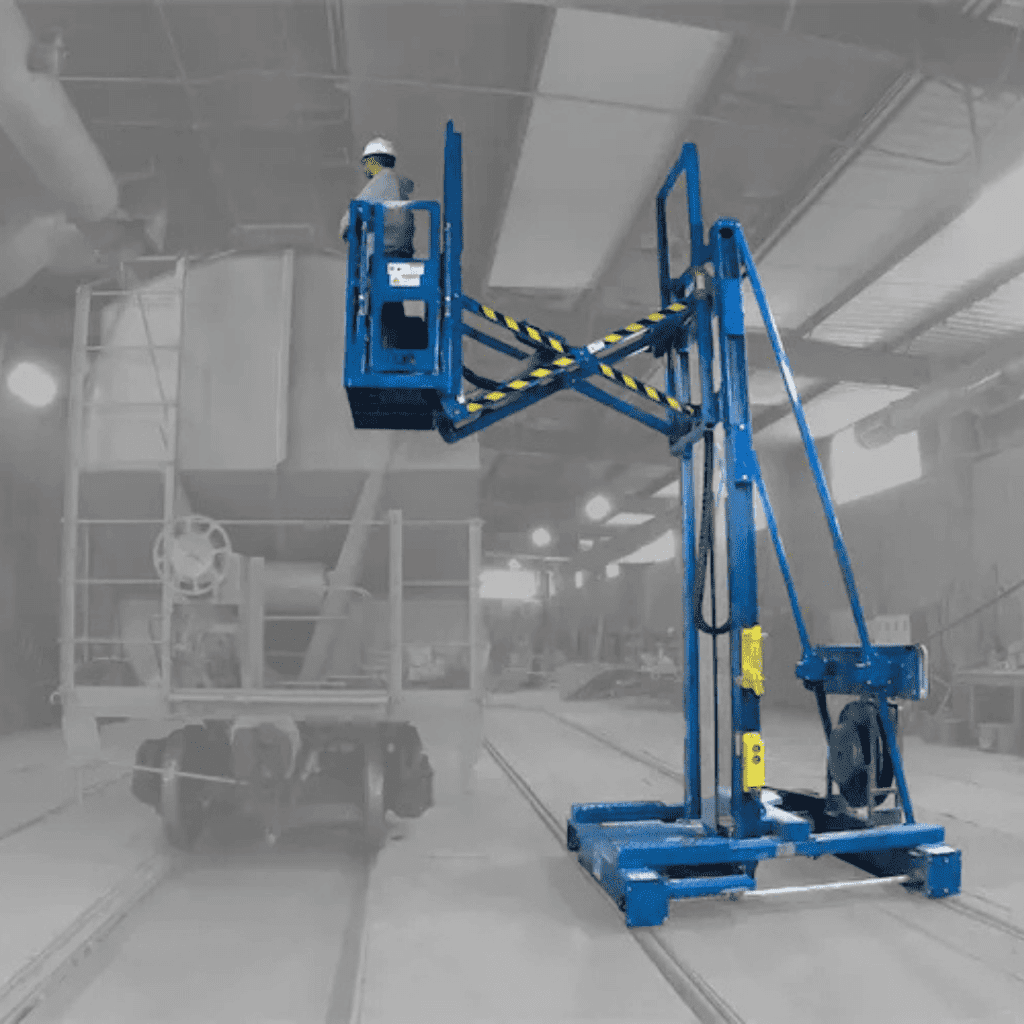 A worker wearing a helmet stands on a blue elevated work platform inside an industrial facility with machinery and tracks on the floor. The background is faded in black and white.