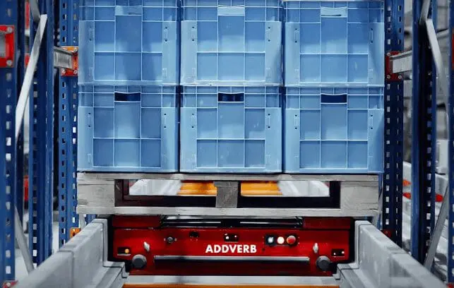 Red pallet shuttle carrying stacked blue totes on a wooden pallet in a racking system.