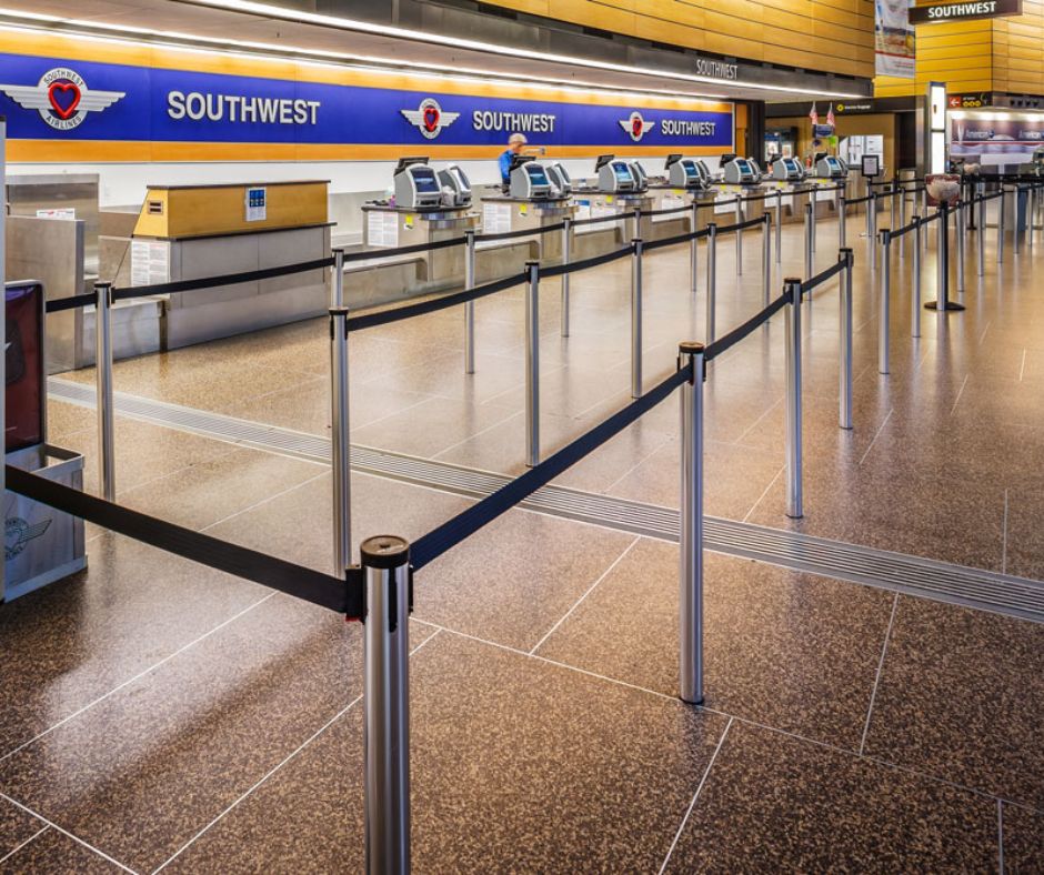 Empty Southwest Airlines check-in counters at an airport, with outdoor retractable belt stanchions guiding the queue and self-service kiosks visible along the counter.