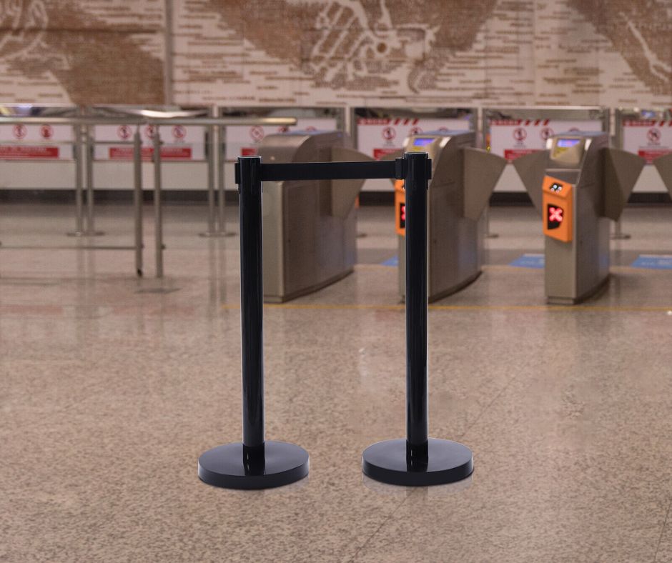 A Visiontron PRIME HD stanchion serves as a retractable barrier in front of closed turnstiles at a transit station, with a world map mural decorating the wall in the background.