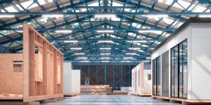 A spacious warehouse with a blue steel roof, large windows, and skylights serves as a hub for assembling prefabricated modular units—ideal for rapid deployment warehouse needs or scalable warehouse facilities.